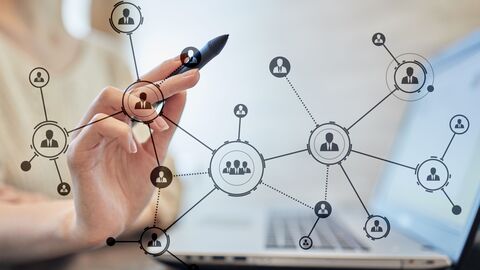 Eine Hand zeichnet ein Netz zur Personalplanung. Im Hintergrund steht ein Laptop.
