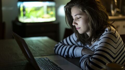 Ein Mädchen sitzt in einem abgedunkelten Raum und schaut sich etwas auf einem Laptop an.