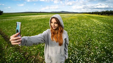Junges Mädchen macht mit einem Handy ein Selfie auf einer grünen Wiese. Junges Mädchen macht mit einem Handy ein Selfie auf einer grünen Wiese.